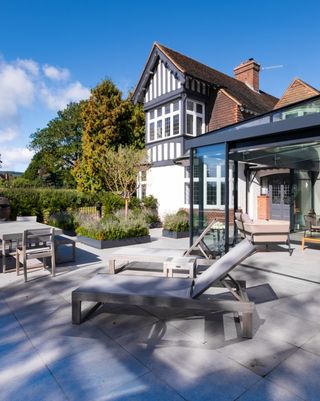 A glass box extension with a paved patio and sun loungers