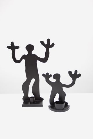Two black candle sticks by IKEA featuring stylized human figurines holding their hands up