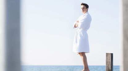 A man standing on a jetty, looking out to sea, wearing one of the best dressing gowns for men