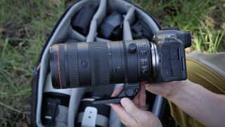 A pair of hands holding a Canon RF 70-200mm f/2.8L IS USM Z lens mounted to a camera, above a camera bag