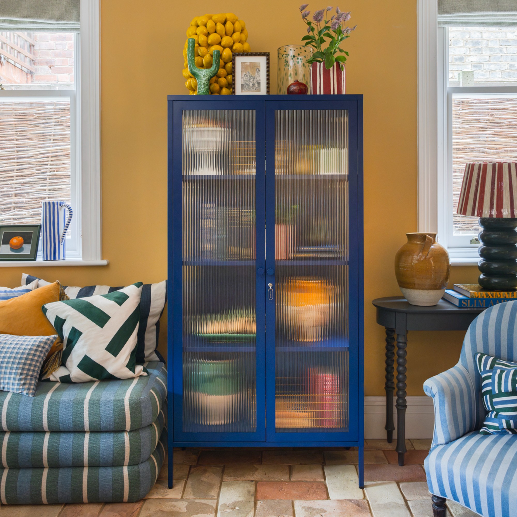 A blue cabinet from Mustard Made's Glass collection in a yellow-painted living room