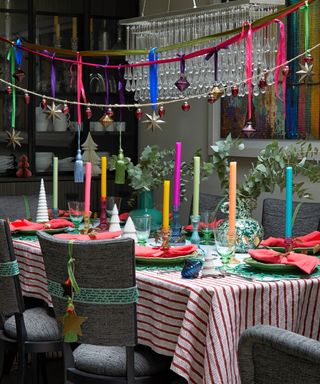 dining room with red and white striped tablecloth, gray chairs, bright candles, green plates, red napkins, hanging decorations