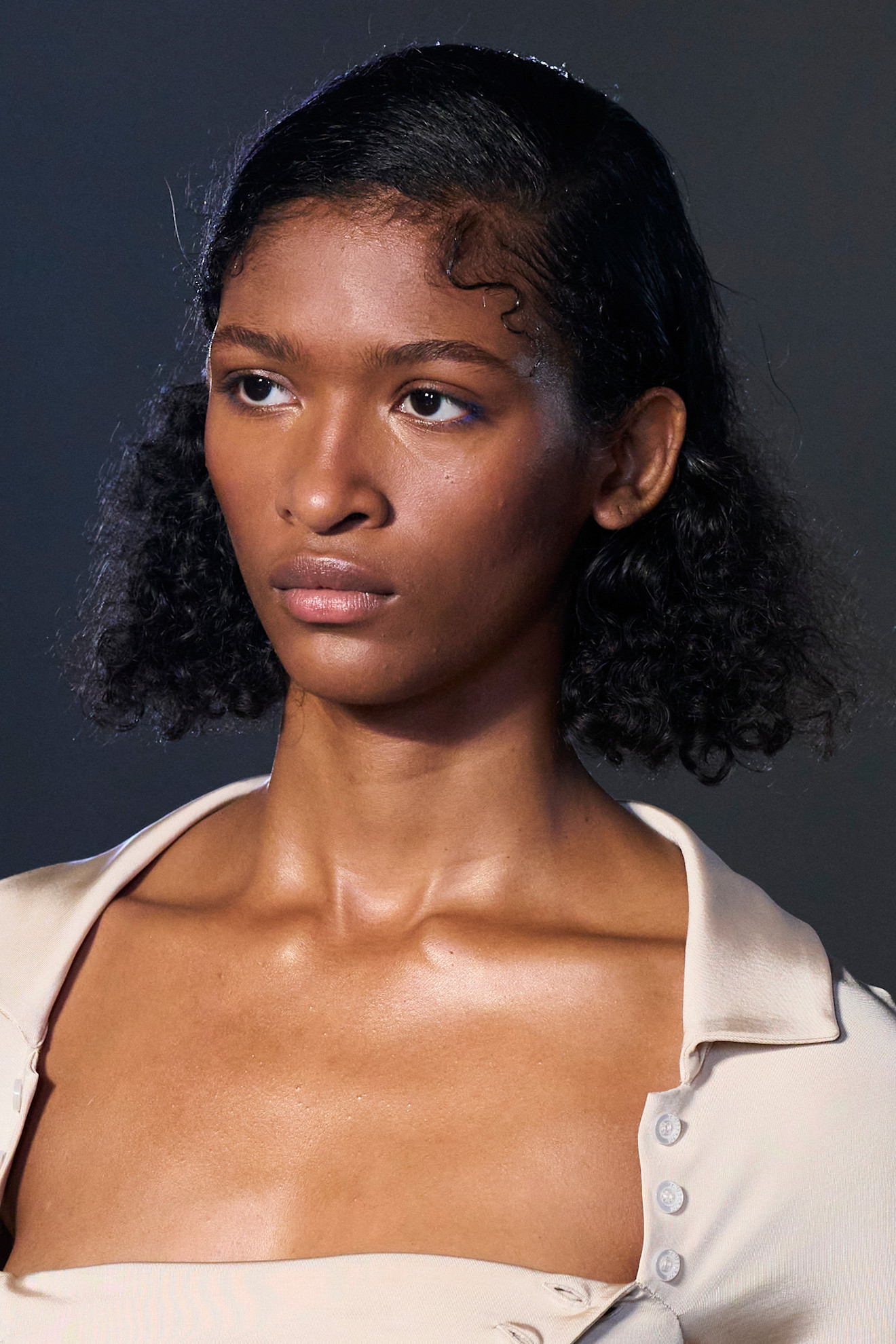 a model with a curly bob and blunt ends with a cream jacket