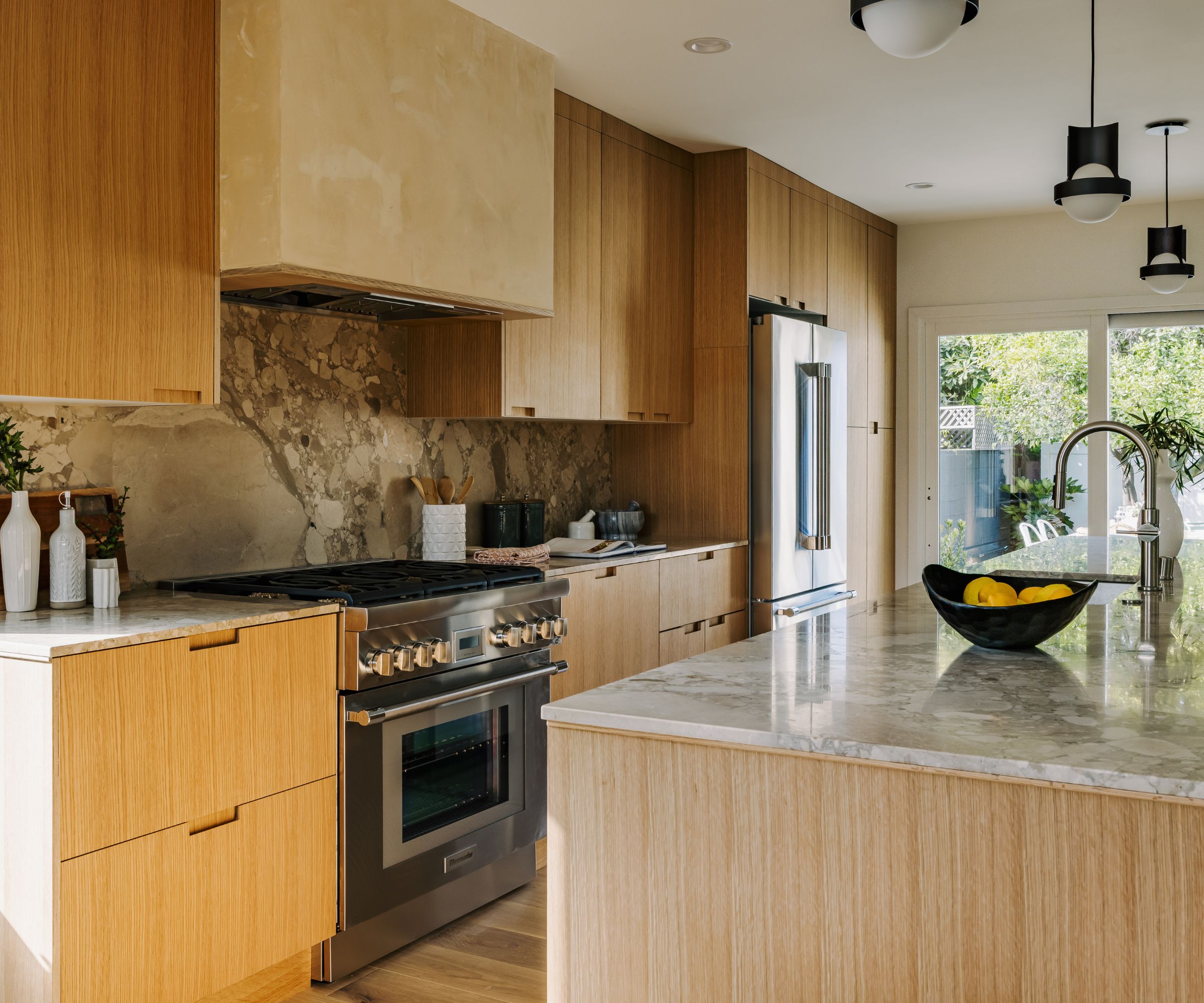 Luxury kitchen featuring light wood cabinetry, a large marble island, a professional stainless steel range, and a textured tan plaster hood.