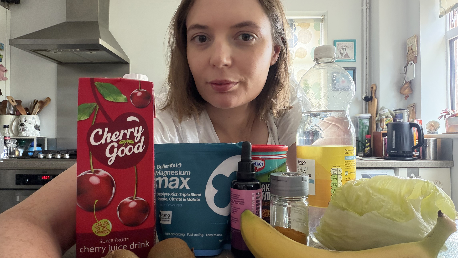 Sleep writer Ruth Jones in her kitchen with a selection of foods and drinks that are meant to be good for sleep, including banana, cherry juice, kiwis, magnesium and turmeric