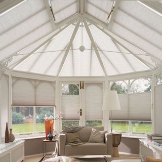 A conservatory with blinds on all windows and a white armchair