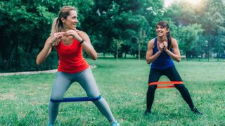 Two women exercising with resistance bands in a park
