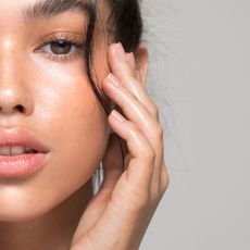 woman with beautiful glowing skin with her hand next to her face 