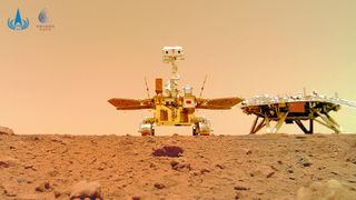 a golden rover and dark-colored lander sit on the red martian surface, with a dusty reddish-brown sky in the background.