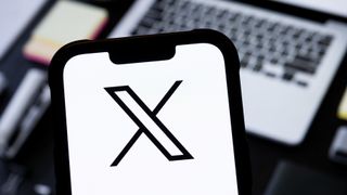 The X logo seen on a smartphone screen in front of a laptop