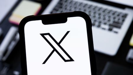 The X logo seen on a smartphone screen in front of a laptop