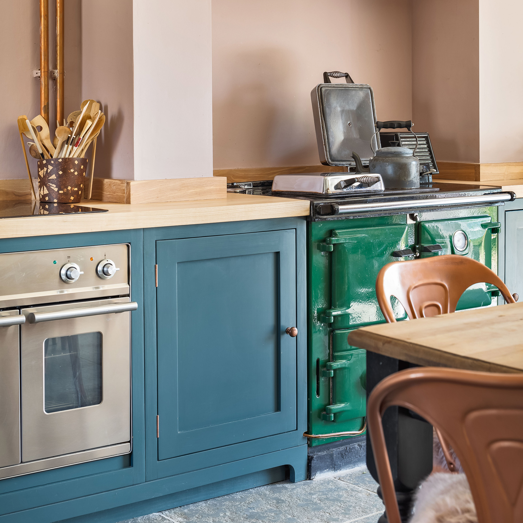 blue painted cabinetry in country kitchen with pink walls and stainless steel oven and green range cooker