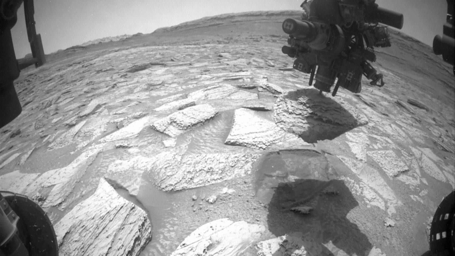A black and white image showing Curiosity's drill stuck in a flat rock.
