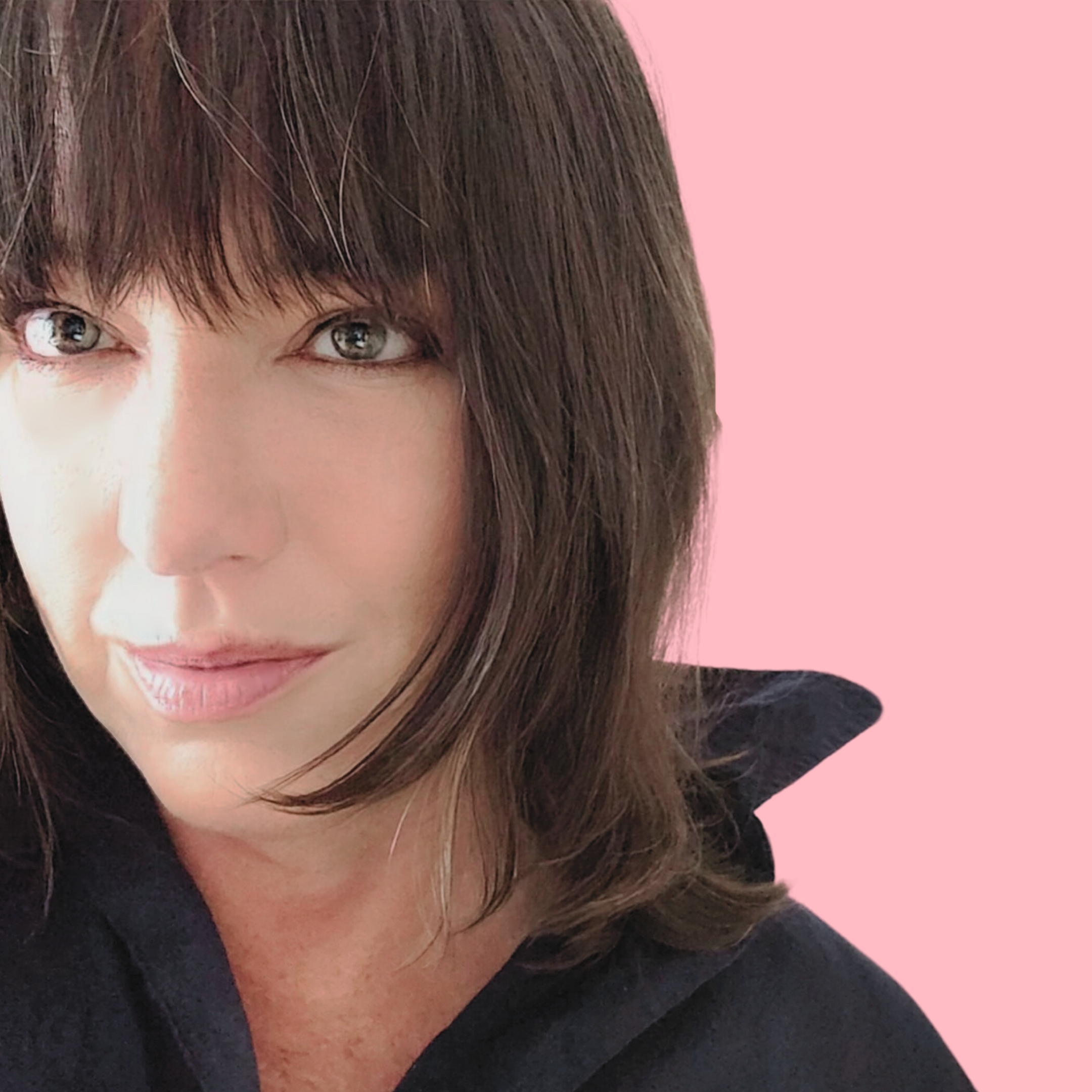 a headshot photo of astrologer Jessica Adams: a lady wearing a black sweater with a dark brown bob and full fringe standing against a pink painted background