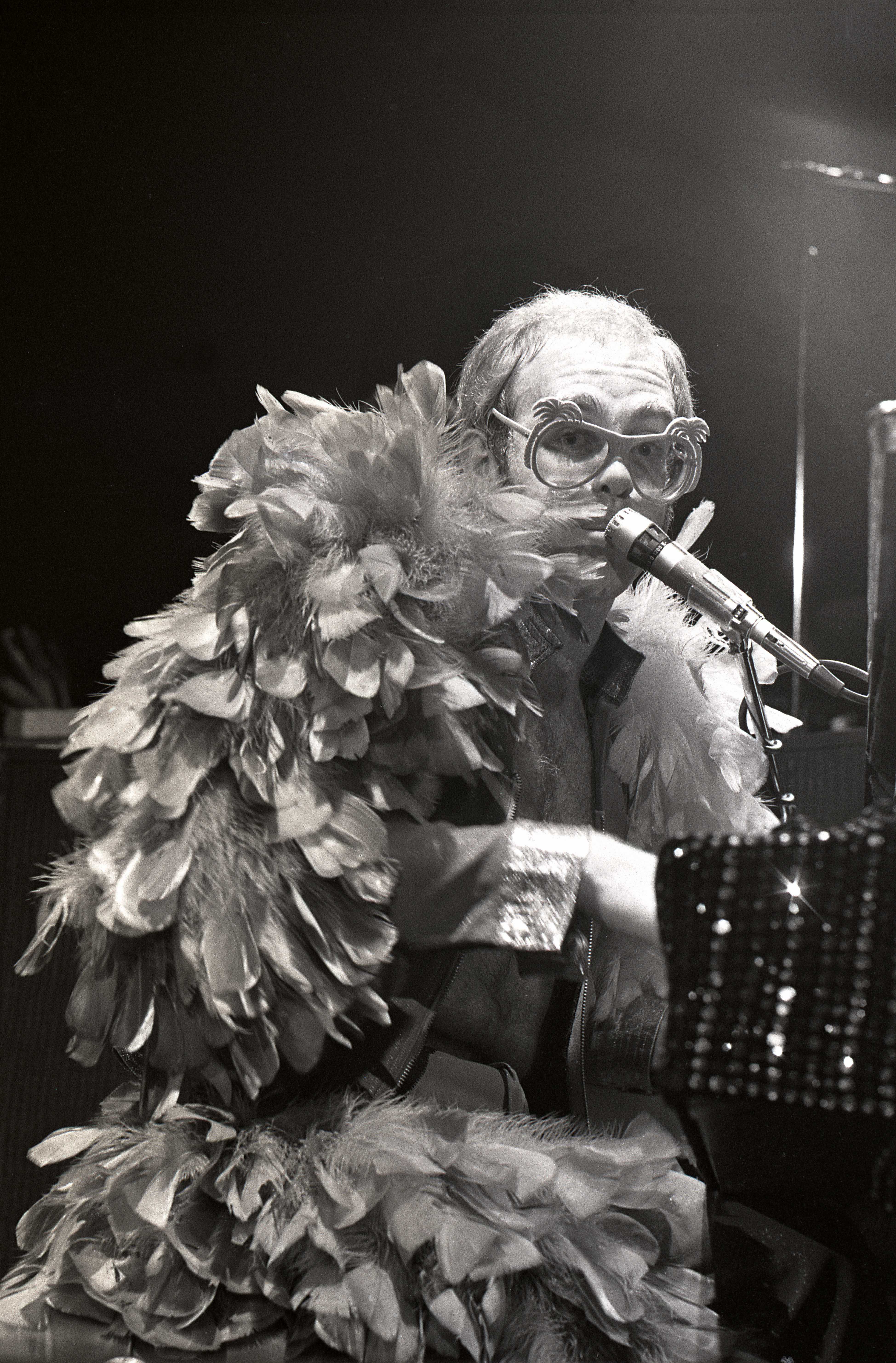 Elton John playing the piano on stage dressed in a feather cape