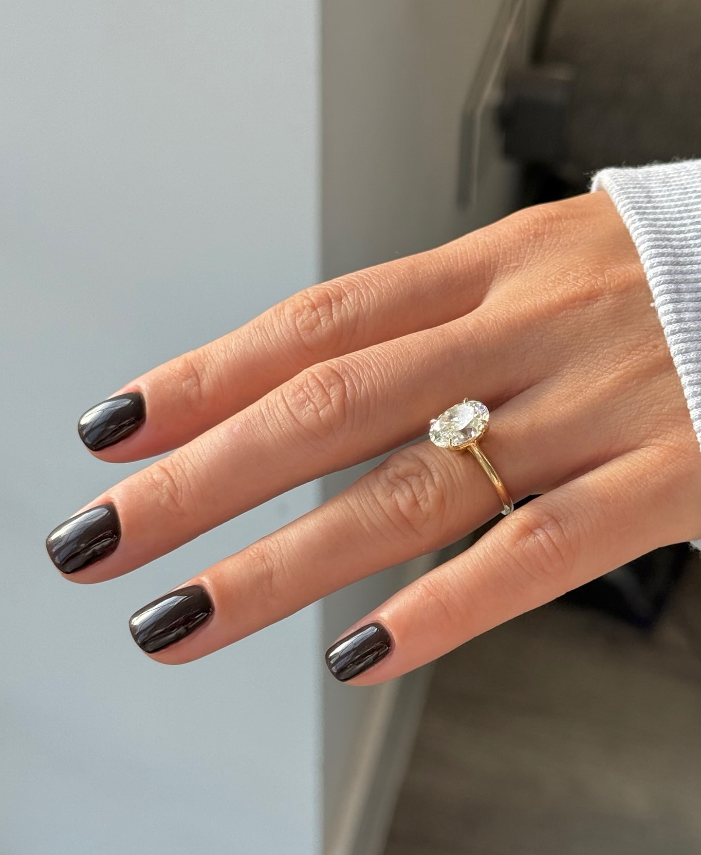 A woman's hand with a diamond engagement ring and a glossy black manicure