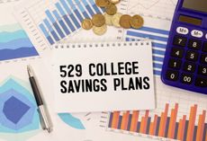 529 College Savings Plan on a notebook next to a calculator, charts and coins.