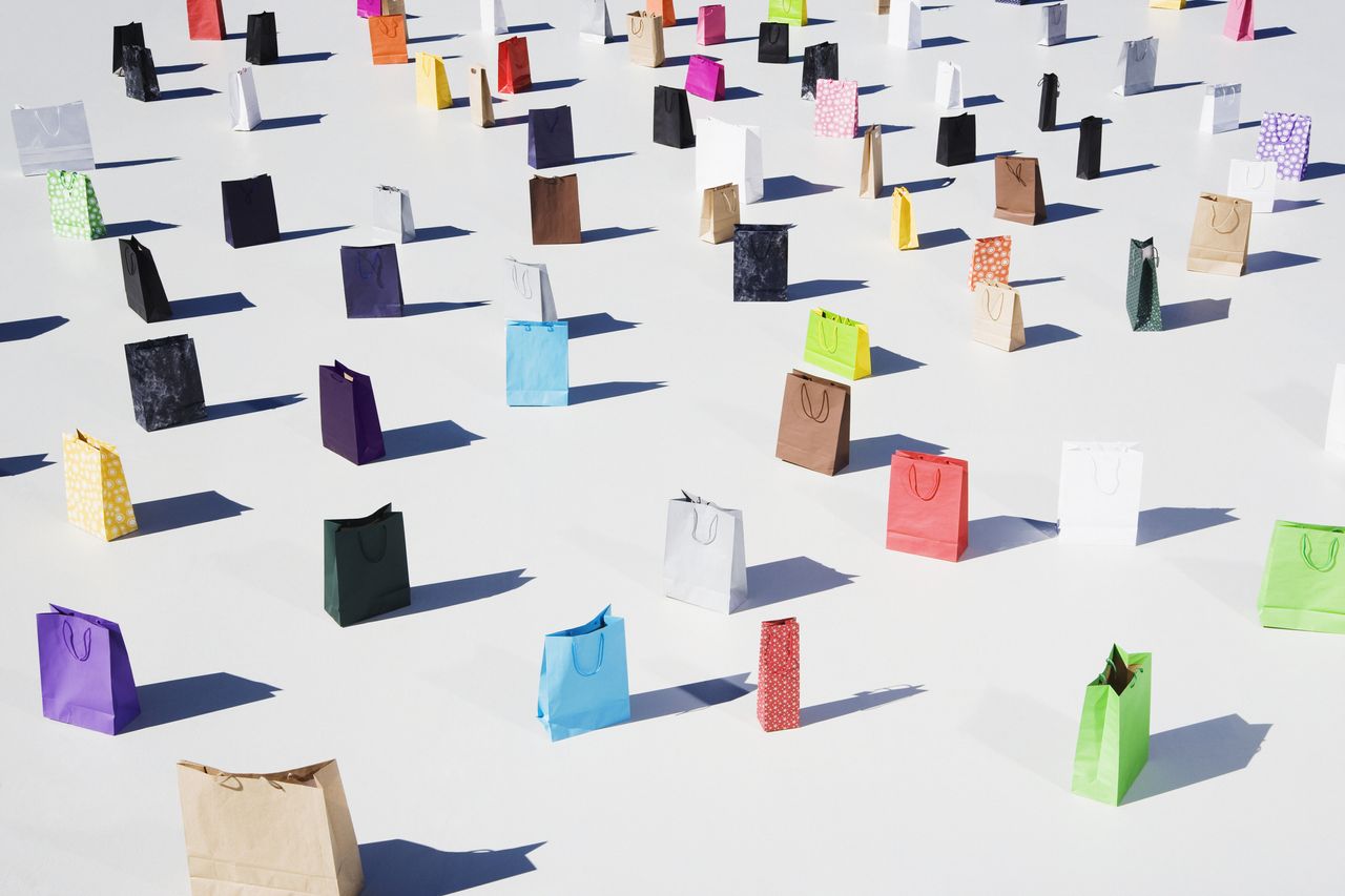 Lots of paper shopping bags in a variety of colors stood upright on a white floor