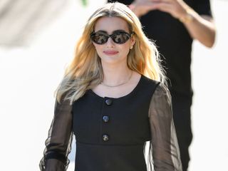 Emma Roberts wears black oval sunglasses and a black dress