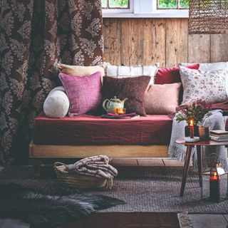 A rustic-style living room with a burgundy settee with scatter cushions in various colours and patterns