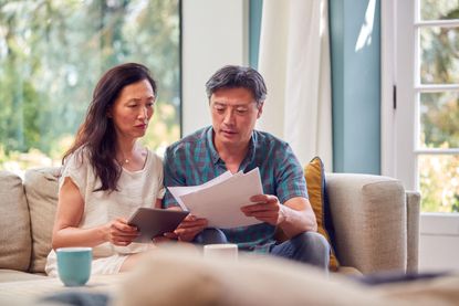 2HMH0NB Mature Couple Sitting On Sofa At Home Reviewing Personal Finances On Laptop