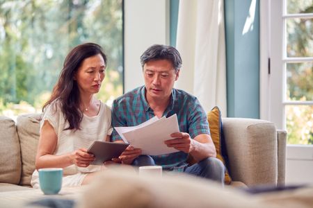 2HMH0NB Mature Couple Sitting On Sofa At Home Reviewing Personal Finances On Laptop