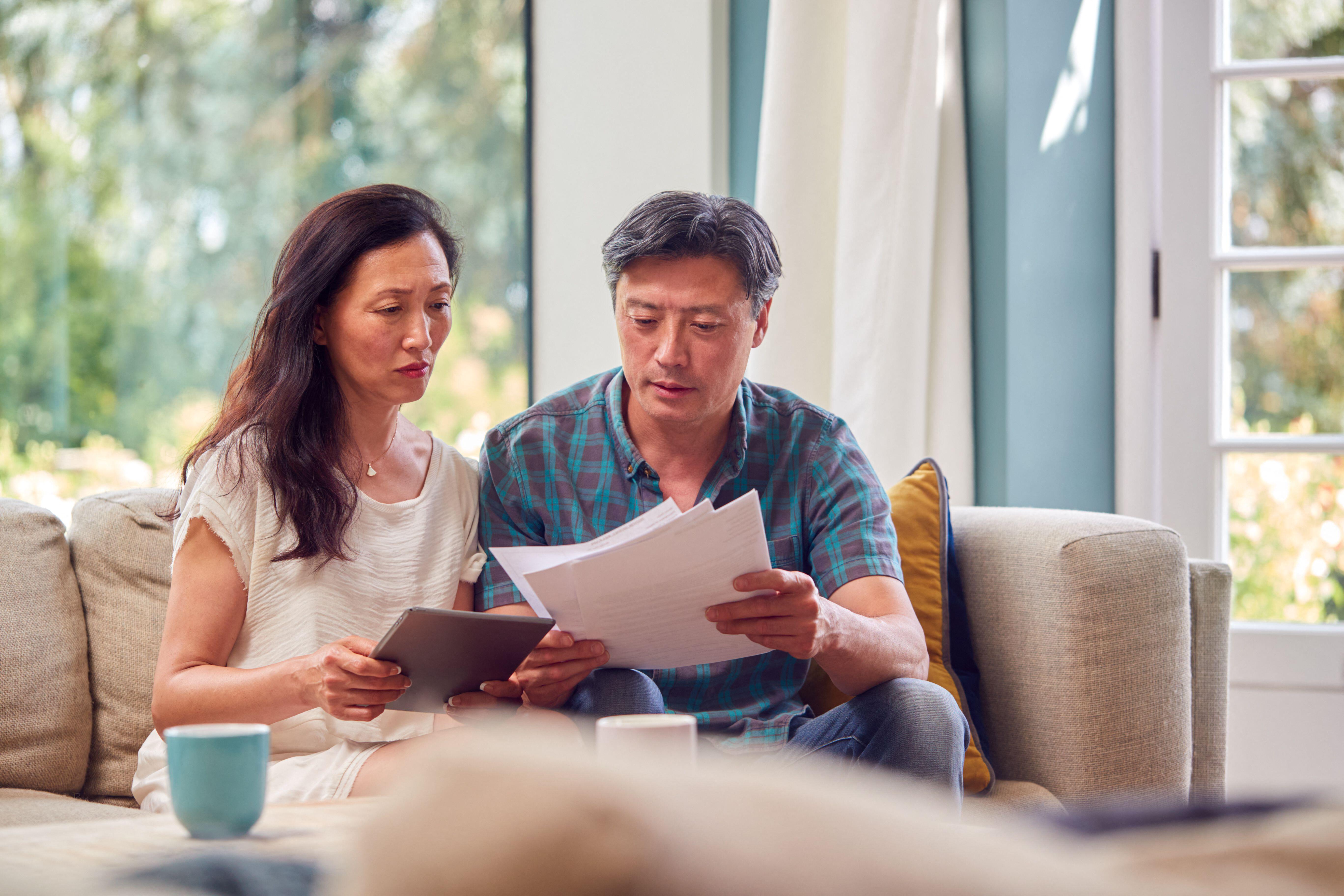 2HMH0NB Mature Couple Sitting On Sofa At Home Reviewing Personal Finances On Laptop