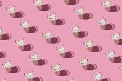Pattern of glass cups filled with milk on pink background.