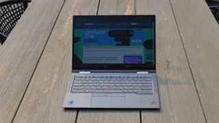 En Lenovo ThinkPad X1 Yoga Gen 6 står öppnad på ett träfärgat trädgårdsbord utomhus.
