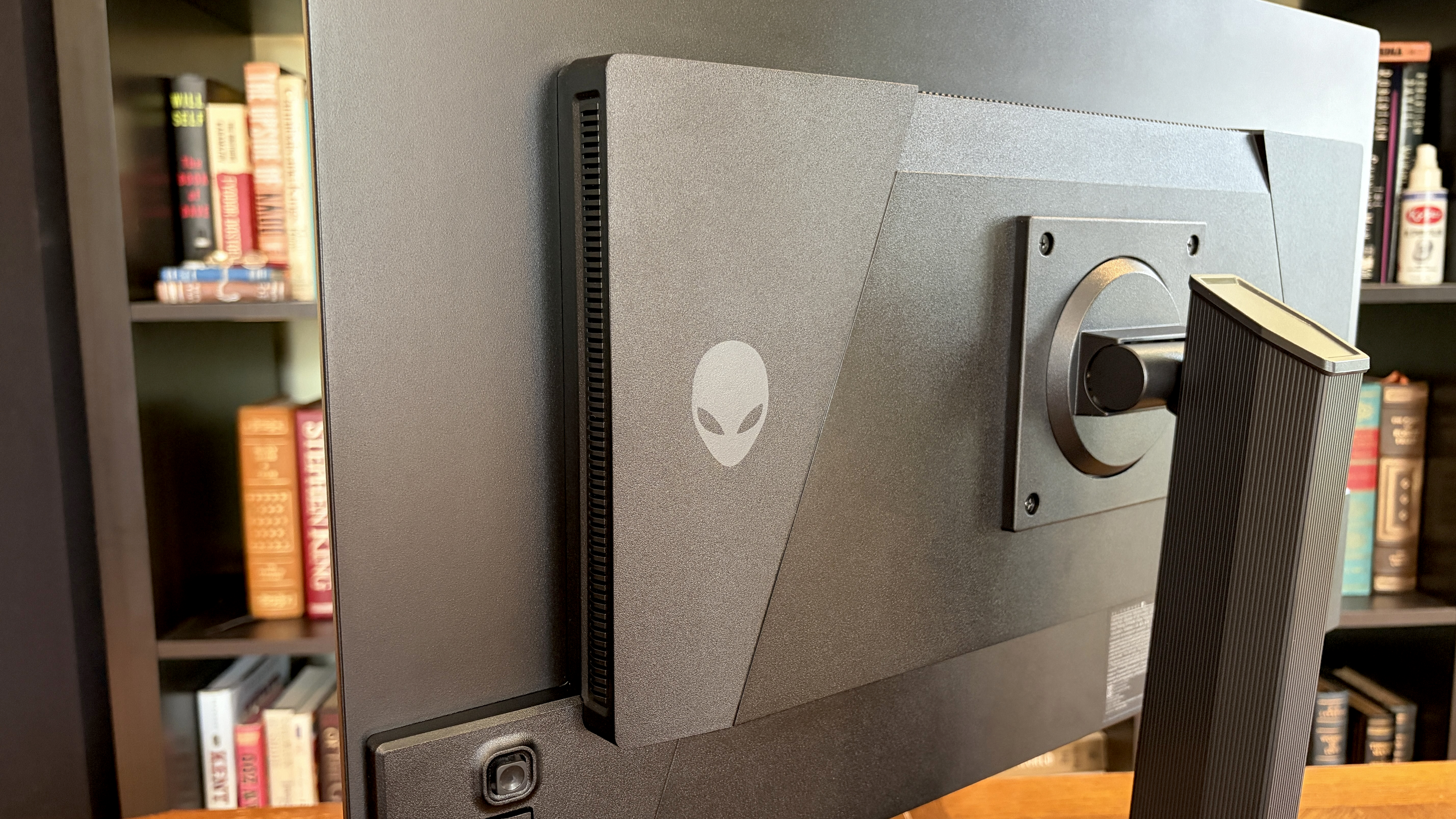 Back of a monitor displaying a stylized alien logo, set in an office with bookshelves filled with various books. The atmosphere is modern and tech-savvy.