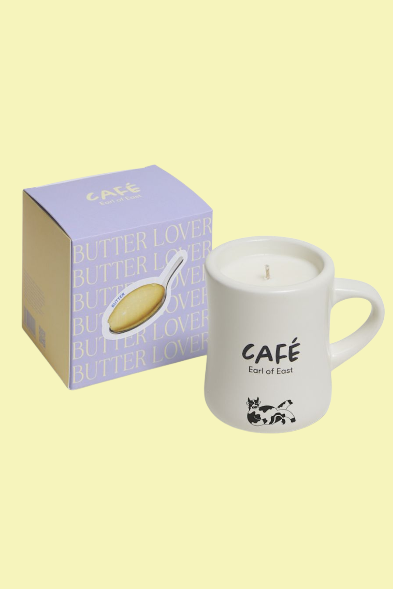 A scented candle in a ceramic mug beside a purple box