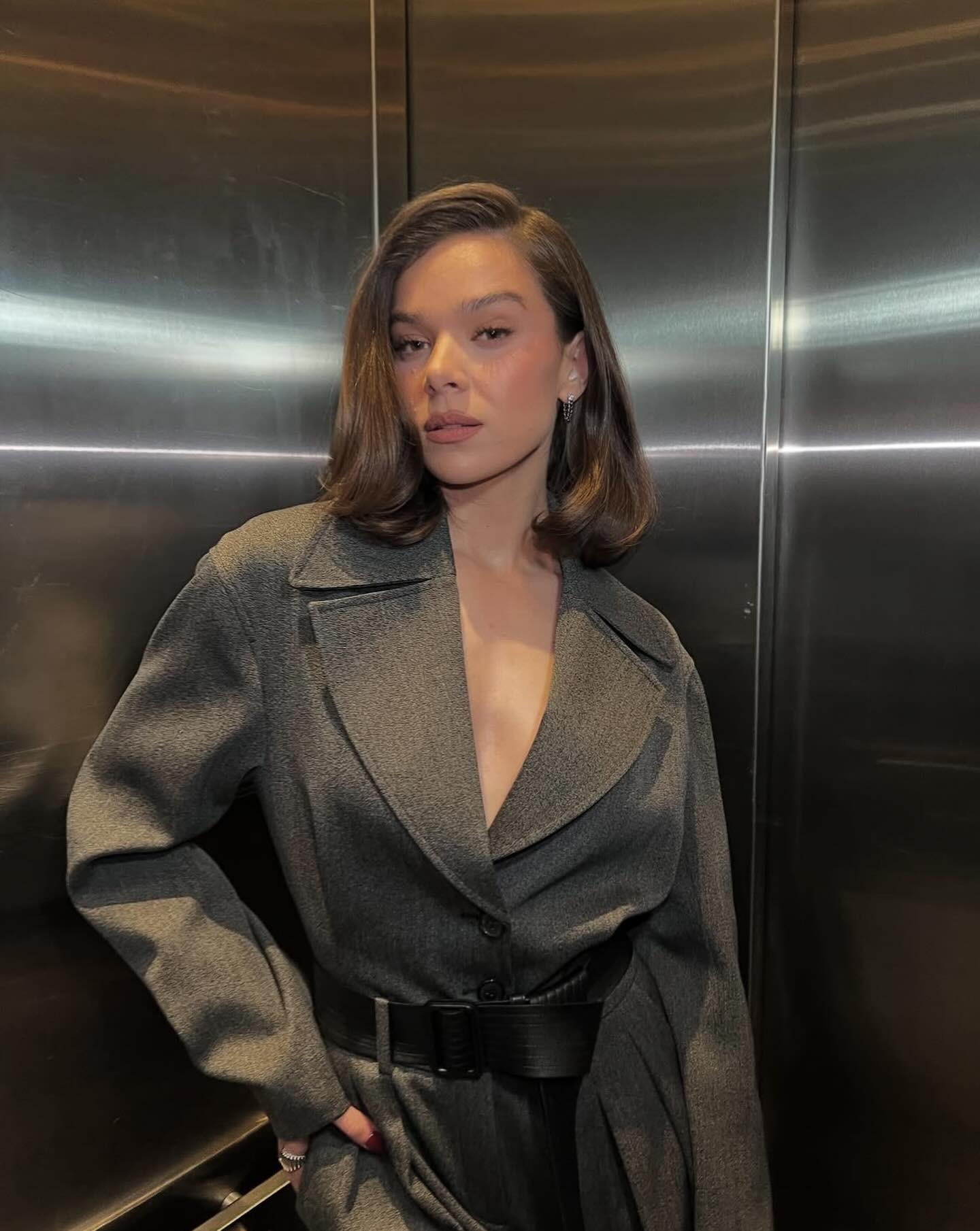 An image of singer and actress Hailee Steinfeld wearing a blazer coat belted at the waist and a side-parted, rounded lob.