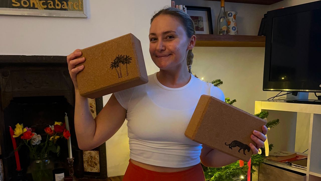 Smiling woman wearing white top holds cork yoga blocks