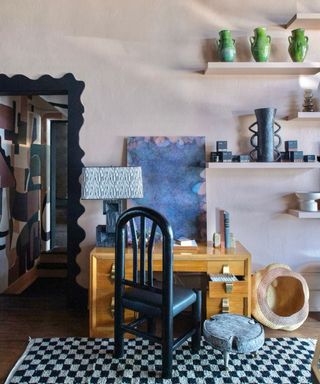 office space with light pink walls, open shelving, wooden desk and black chair with checkered rug