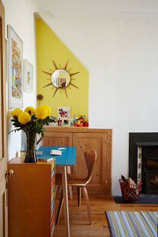 Mid-century home office in the living room, with wooden furniture, a wooden floor, a yellow feature wall and a green and blue rug