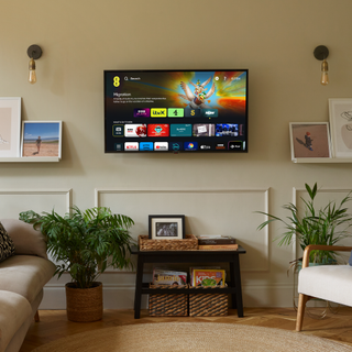 Beige wall with flat screen tv and wall lights either side, and houseplants on the wooden floor beneath