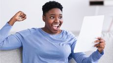 A young woman celebrates while she looks at a letter while sitting on her sofa.