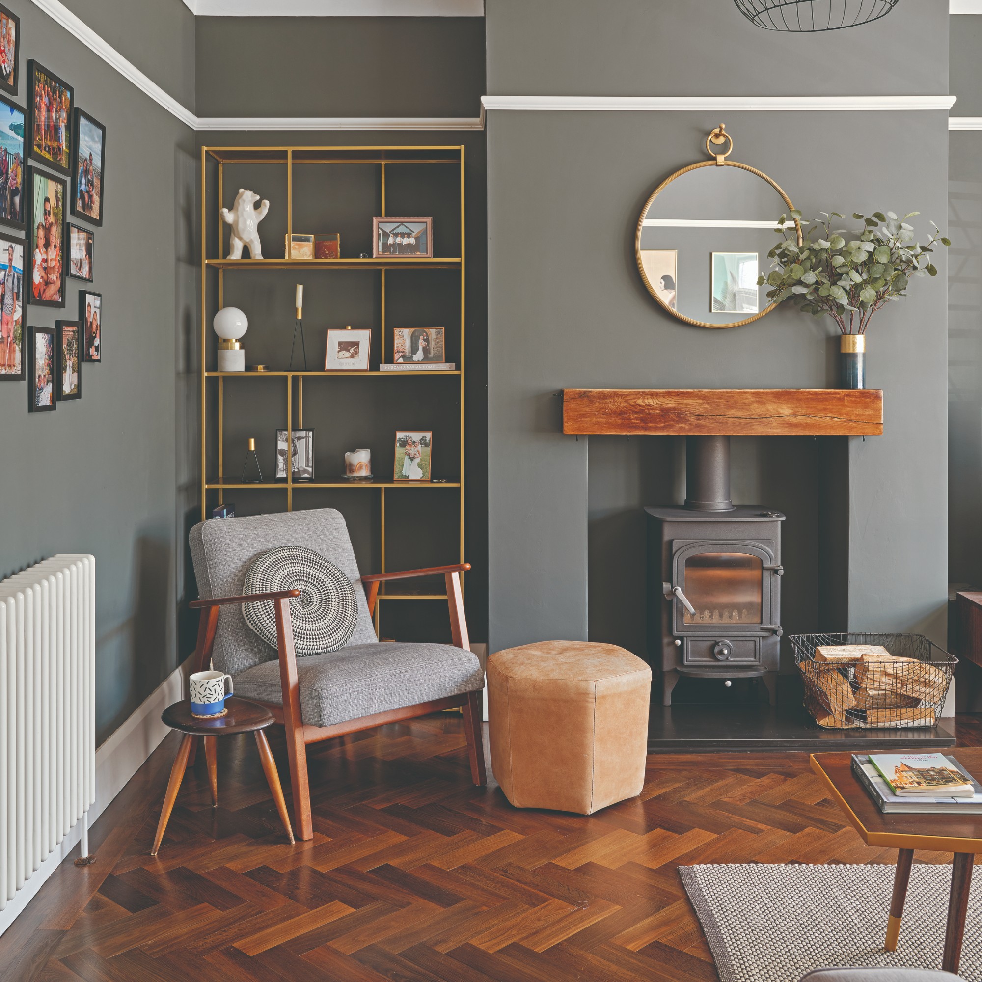 A grey living room with a grey accent chair, wooden floors and a photo gallery wall