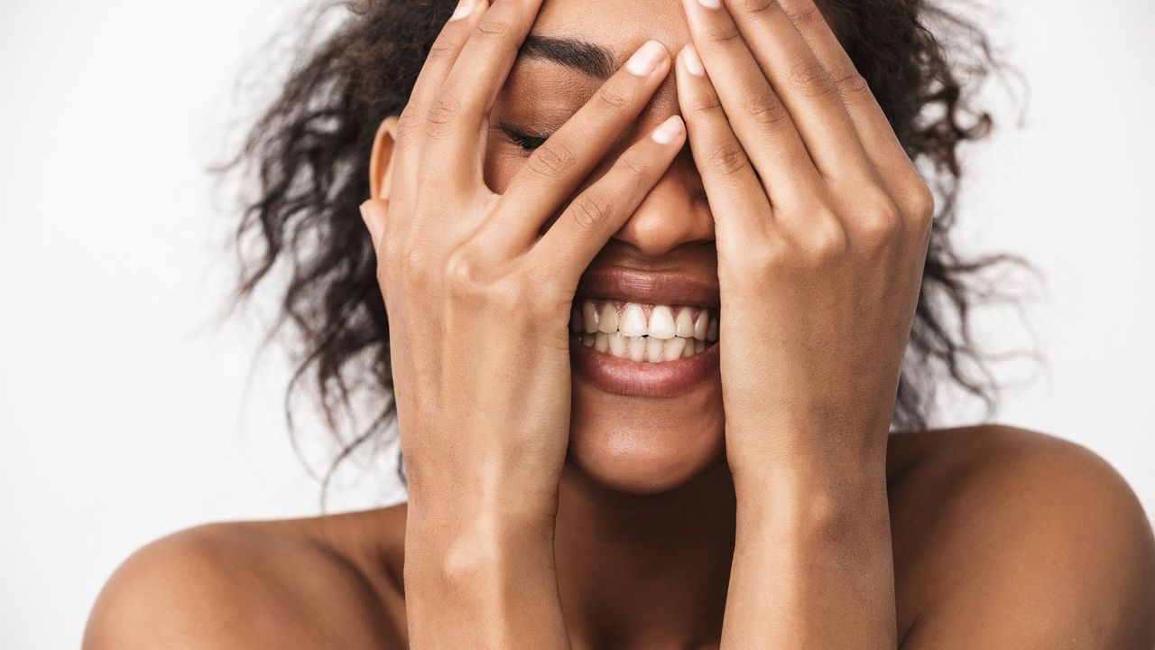 Image of a smiling woman with fresh, clean skin holding her hands over her face