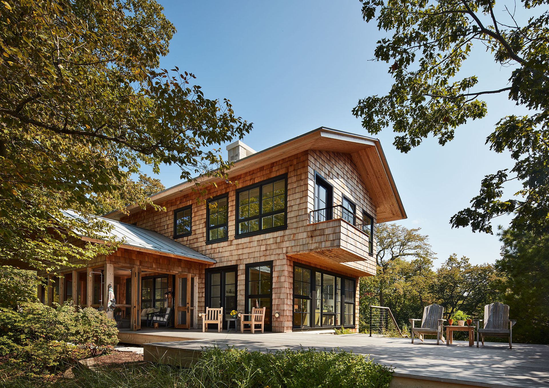 Lakefront cabin with cedar siding and large deck and lower covered porch surrounded by trees