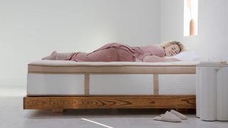 A blonde haired woman in pink pajamas lies on top of the Saatva HD mattress