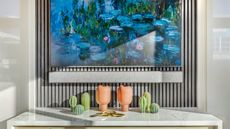 Soundbar and TV showing watercolor art mounted on paneled wall, above marble surface with artificial cacti and pots.