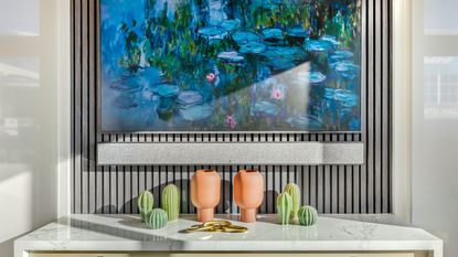 Soundbar and TV showing watercolor art mounted on paneled wall, above marble surface with artificial cacti and pots.