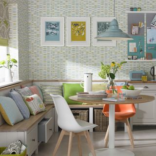 small dining room with bench seating in corner, wallpaper, round table, artwork, colourful cushions, blue pendant light, blind, storage under bench
