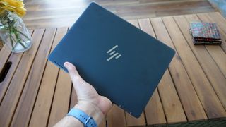 HP Elite Dragonfly Chromebook held in a hand above a wooden table