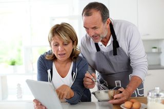 A couple cooks together while checking a recipe on their tablet.