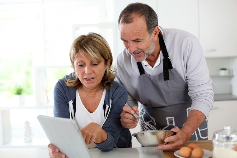 A couple cooks together while checking a recipe on their tablet.