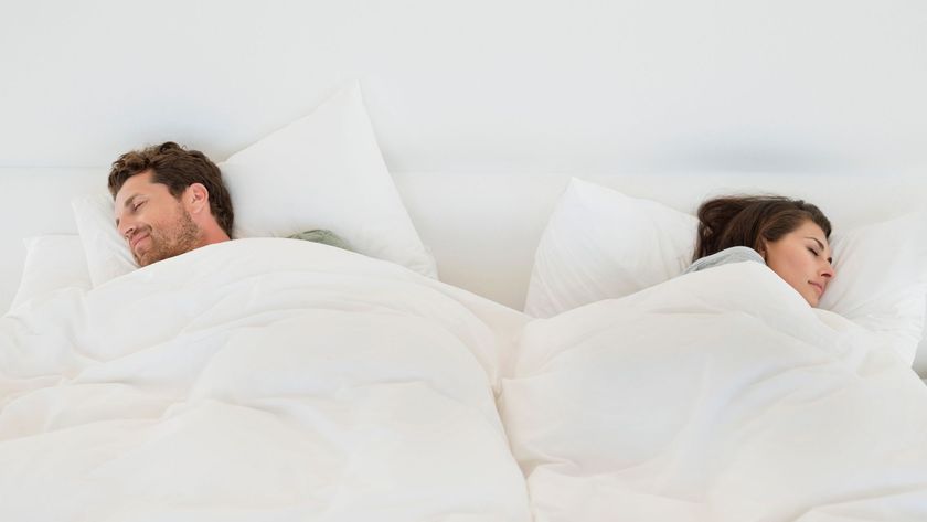 A couple sleeping on their sides facing the opposite way with two separate duvets