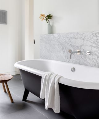 A bathroom with a marble splashback and large black bathtub with feet