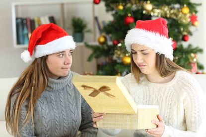 Disappointed woman receiving a gift from a frustrated friend in christmas at home